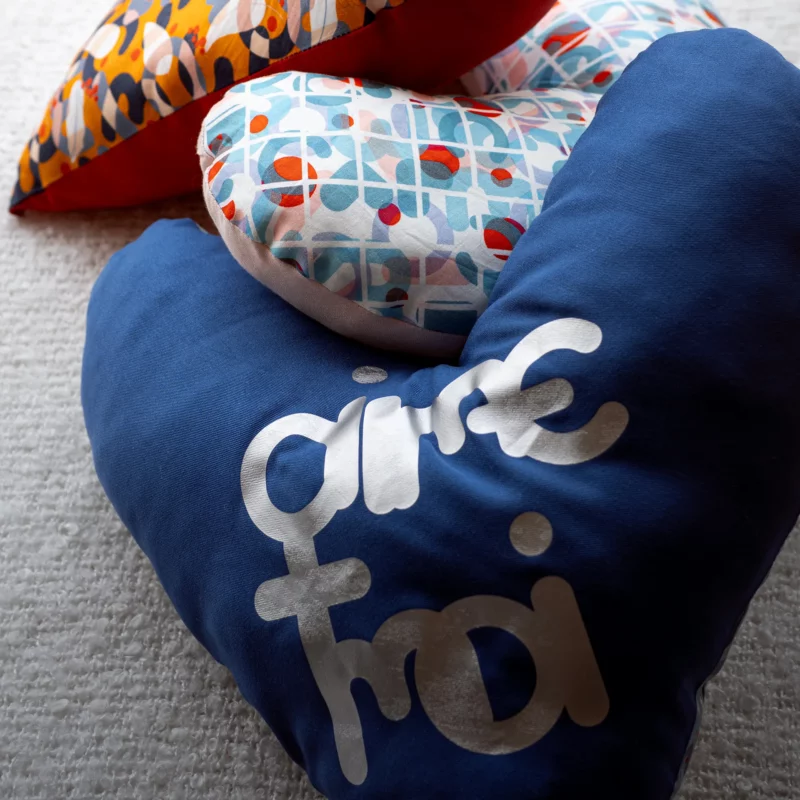 Coussin cœur post-mastectomie posé sur un lit, modèle Qi-Bô avec message
